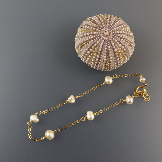 Pearl bracelet with gold chain on a textured gray background