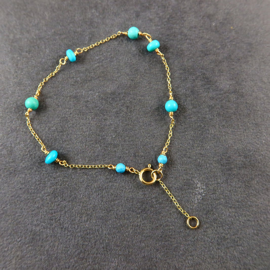 Gold bracelet with turquoise beads on a gray background