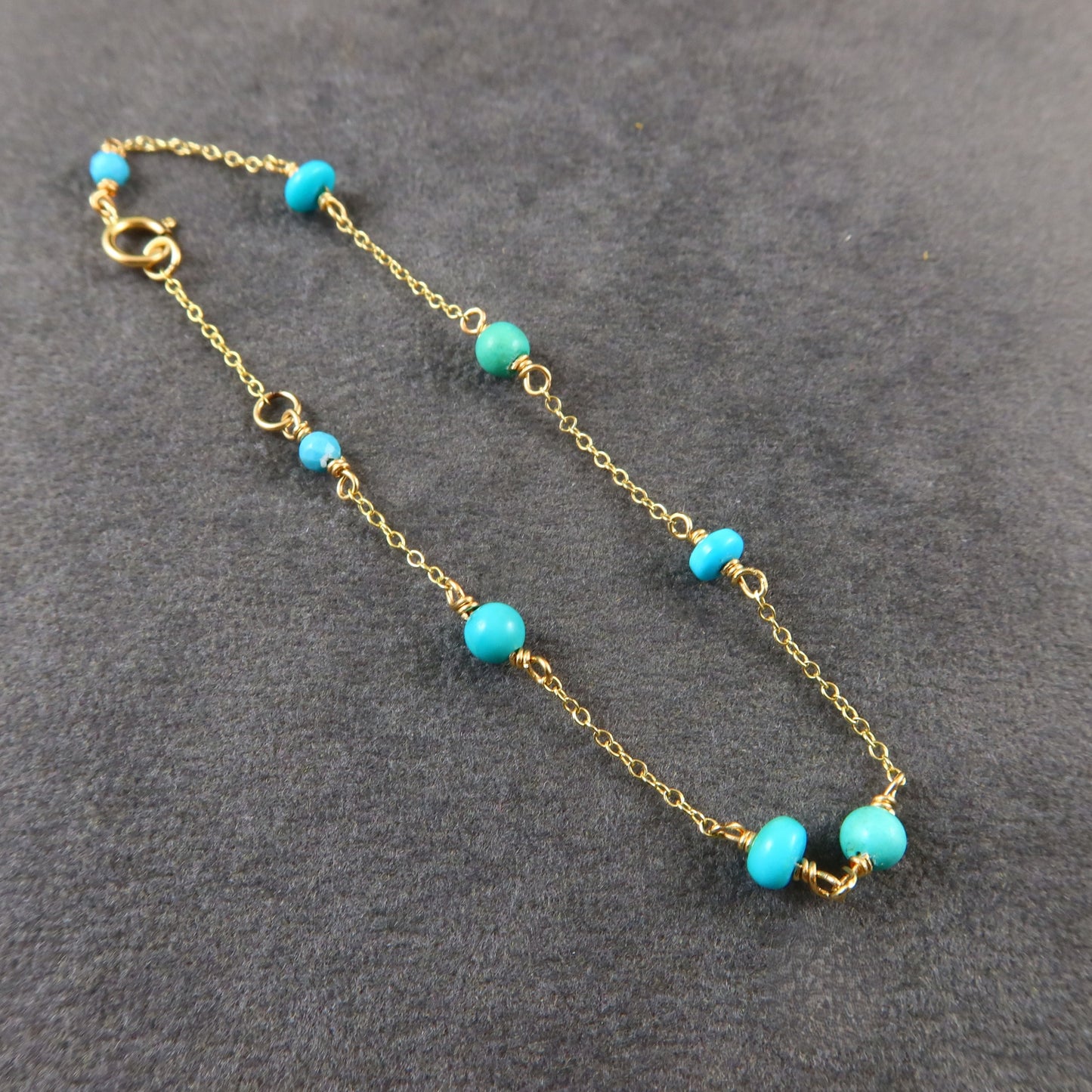 Gold chain bracelet with turquoise beads on a gray surface
