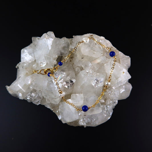 Gold bracelet with blue beads on a crystal rock against a black background