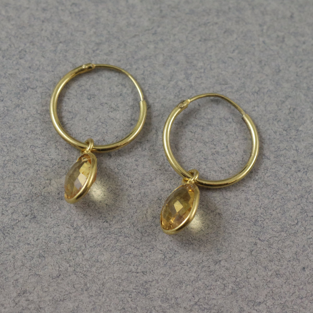 A pair of faceted citrine gemstone earrings with gold vermeil hooks displayed on a grey earring stand.