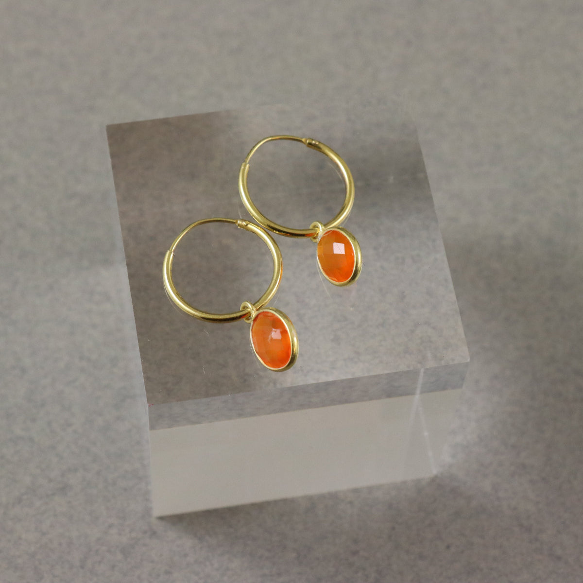 A pair of gold vermeil hoop earrings with faceted carnelian gemstones displayed on a grey velvet stand.