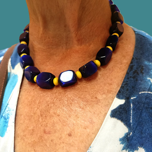 Necklace with blue and yellow beads worn by a person against a blue background