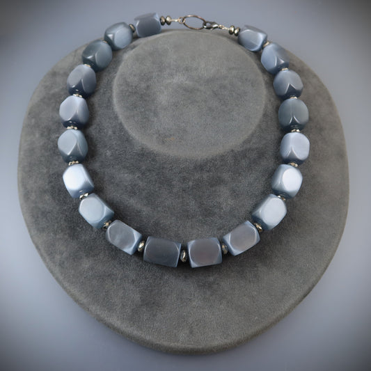 Necklace with gray and white beads on a gray surface