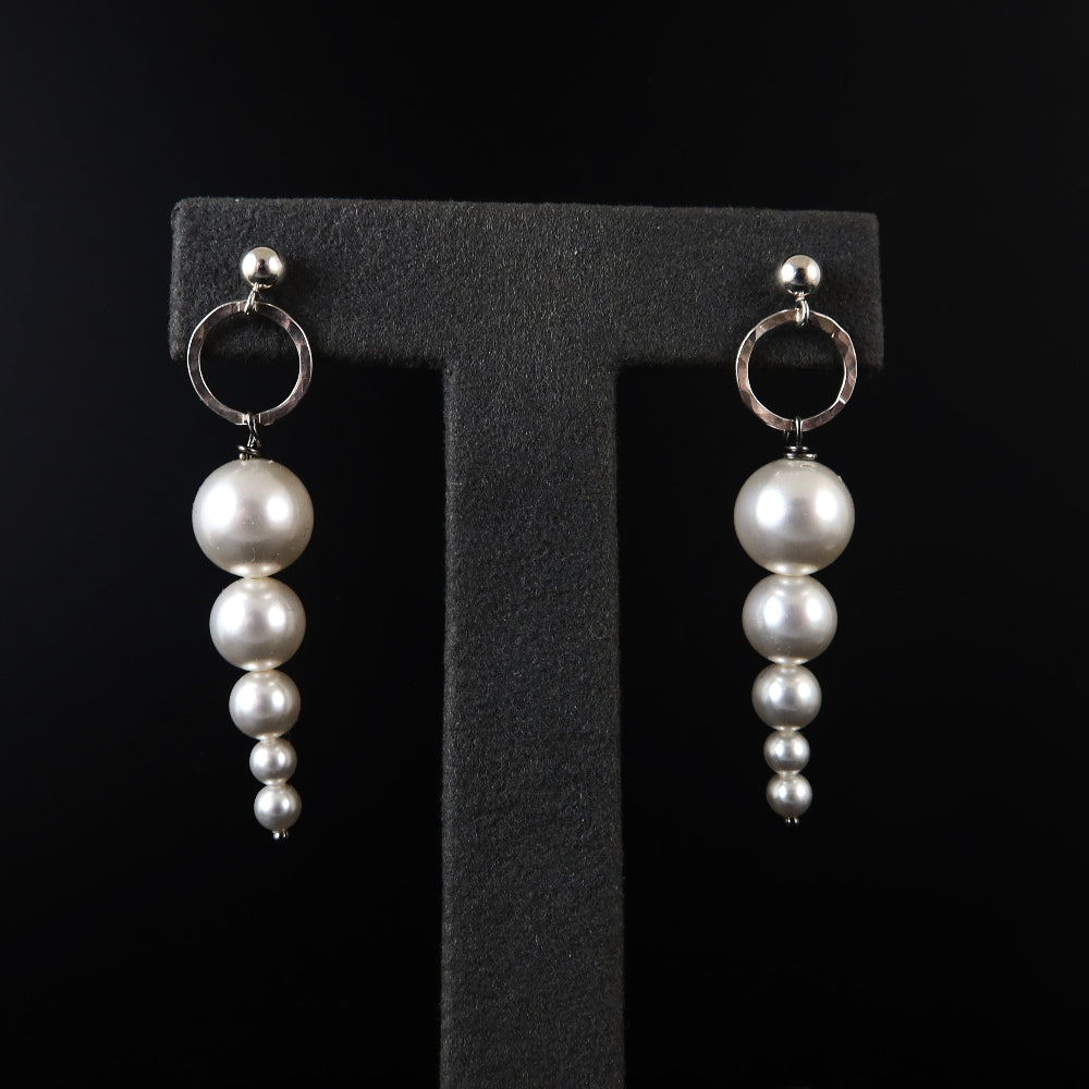 Pair of pearl earrings on a black letter 'T' stand.
