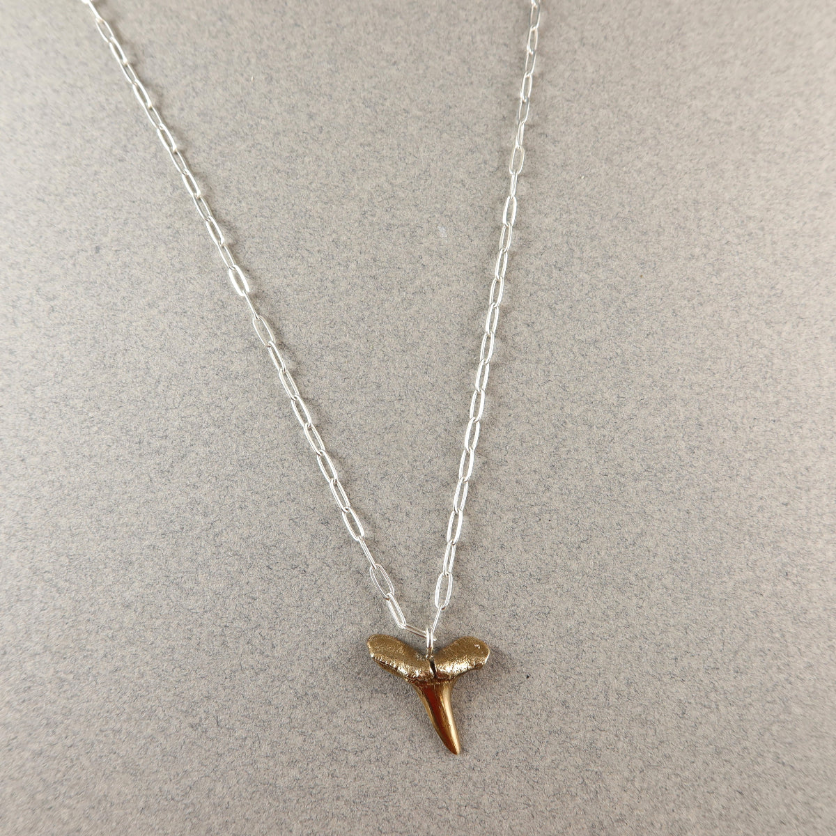 Necklace with a gold shark tooth pendant on a light gray background