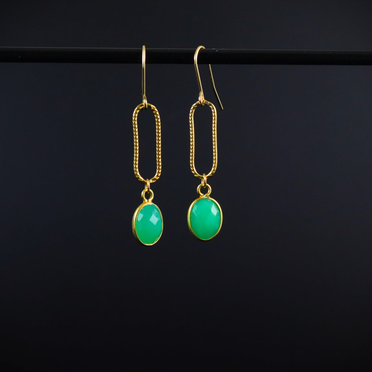 Gold earrings with green gemstones on a black background