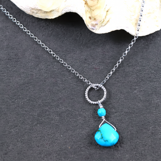 Necklace with turquoise pendant and silver chain on a dark surface
