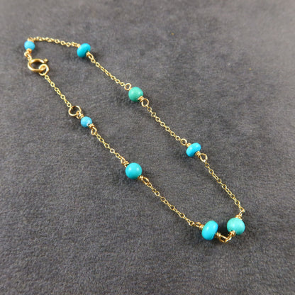 Gold chain bracelet with turquoise beads on a gray surface