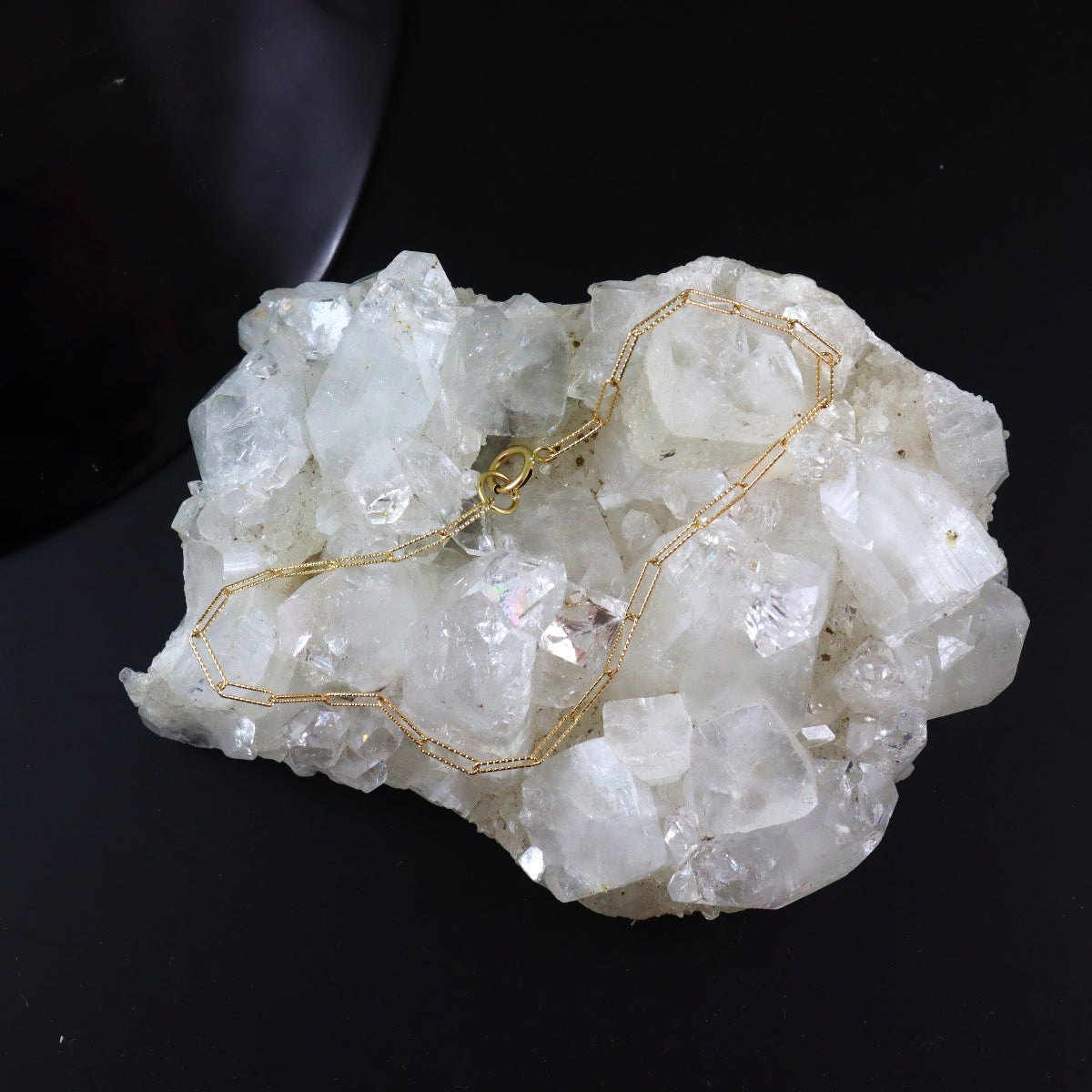 Gold necklace draped over a crystal rock on a black background