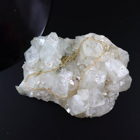Gold necklace draped over a crystal rock on a black background