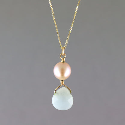 A delicate gold chain necklace featuring a dual pendant design: a round, lustrous pale pink pearl on the top and a faceted, teardrop-shaped light blue stone on the bottom, both set in gold.