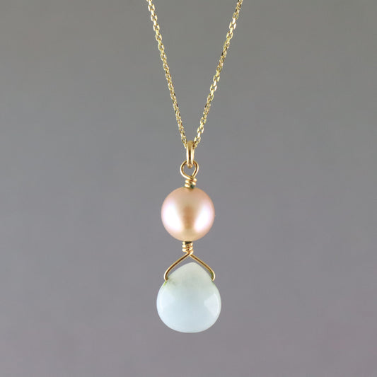 A delicate gold chain necklace featuring a dual pendant design: a round, lustrous pale pink pearl on the top and a faceted, teardrop-shaped light blue stone on the bottom, both set in gold.