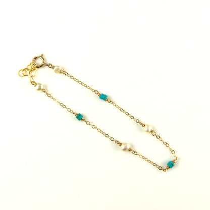 Gold chain bracelet with pearls and turquoise beads on a white background