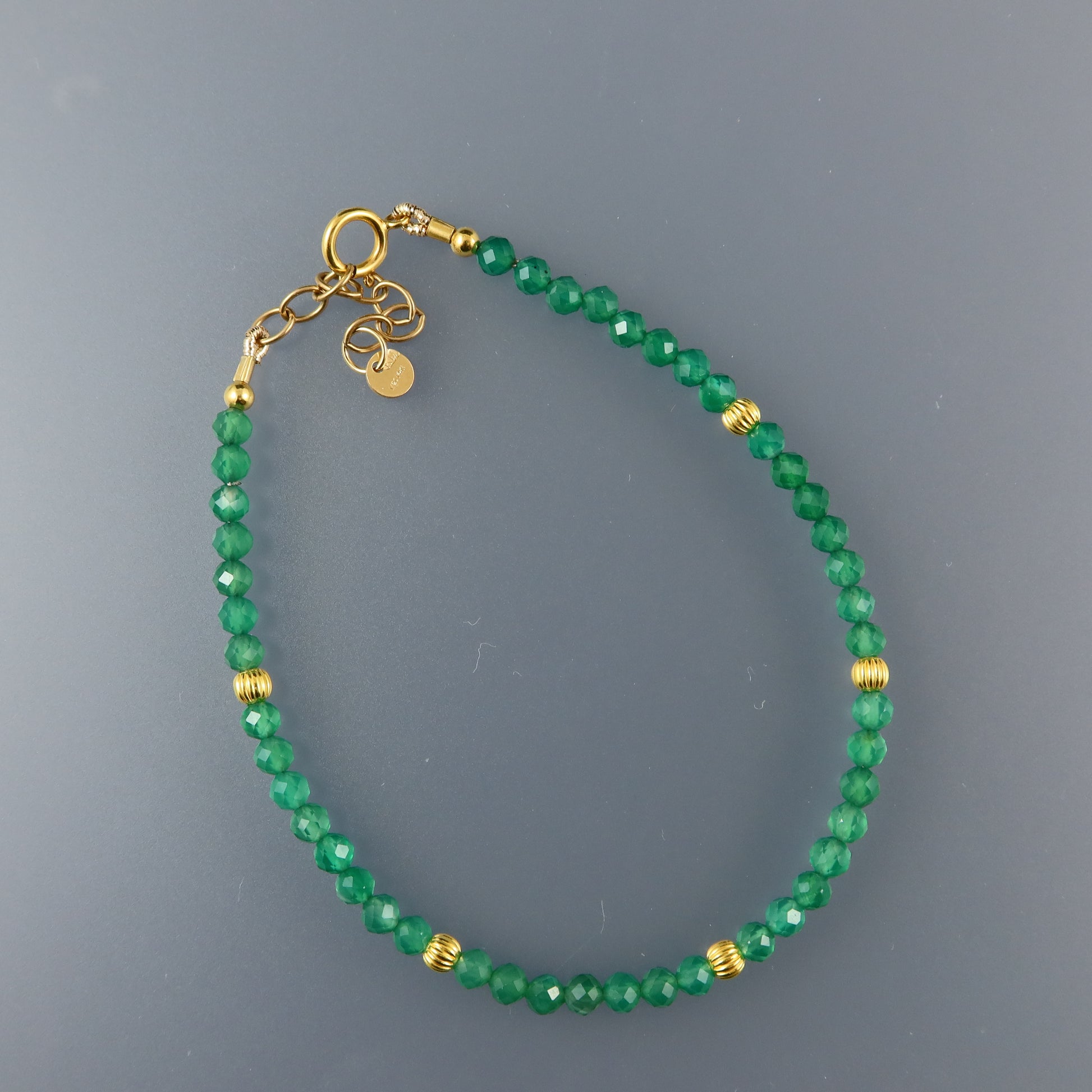 Green beaded bracelet with gold accents on a gray background