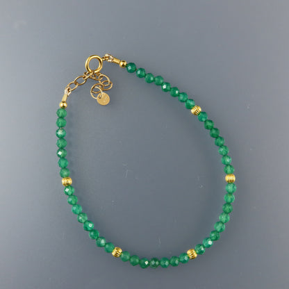 Green beaded bracelet with gold accents on a gray background