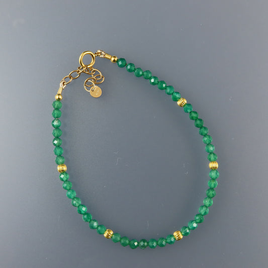 Green beaded bracelet with gold accents on a gray background