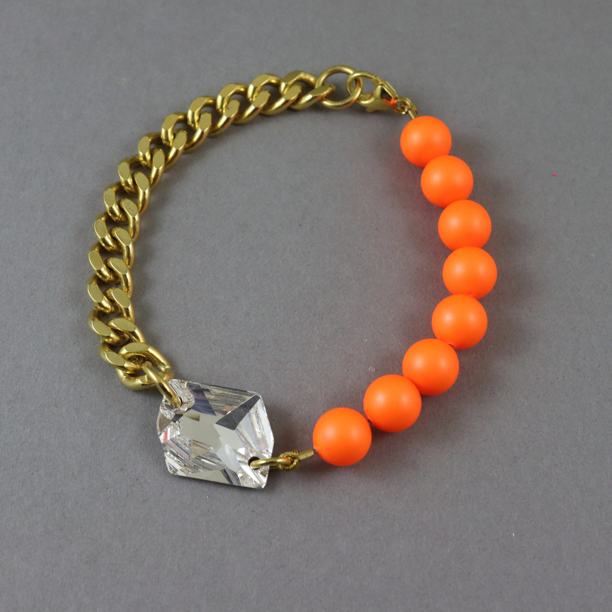 A gold-tone chain bracelet with a row of bright orange round beads and a faceted clear crystal charm, displayed on a neutral gray background.