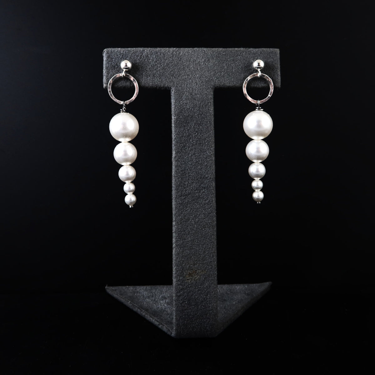 Pearl earrings on a black T-shaped stand against a black background