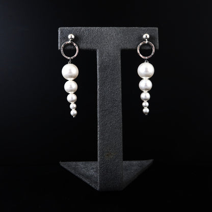 Pearl earrings on a black T-shaped stand against a black background