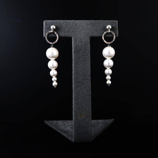 Pearl earrings on a black T-shaped stand against a black background