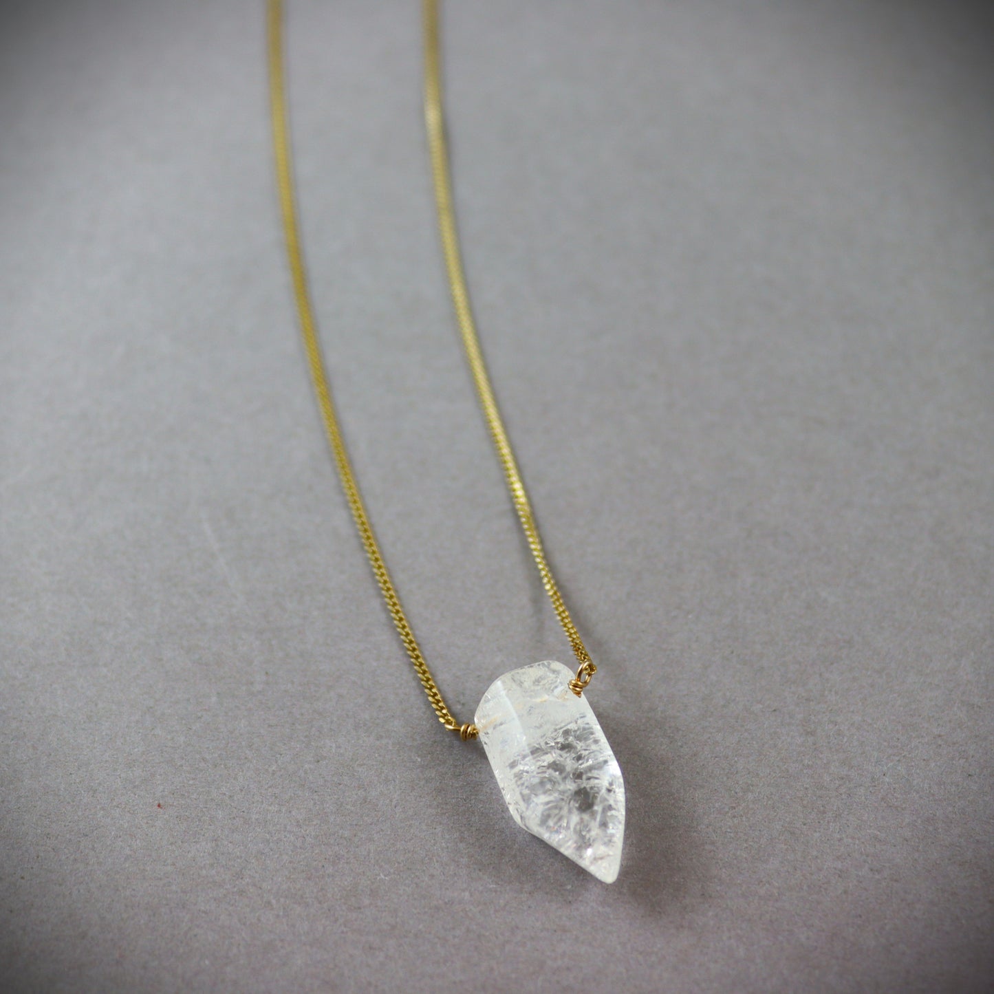 Gold filed  chain Necklace with a clear crystal quartz pendant on a dark gray background