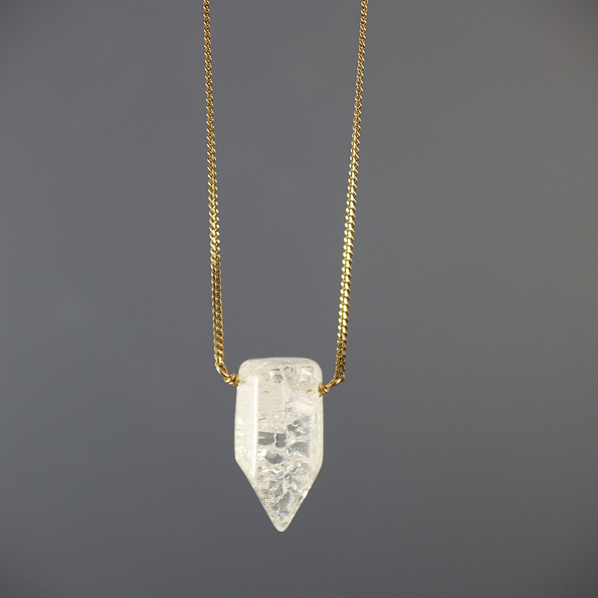 Gold filed  chain Necklace with a clear crystal quartz pendant on a dark gray background